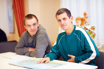 Cheerful adult men with disability sitting at the desk in rehabilitation center